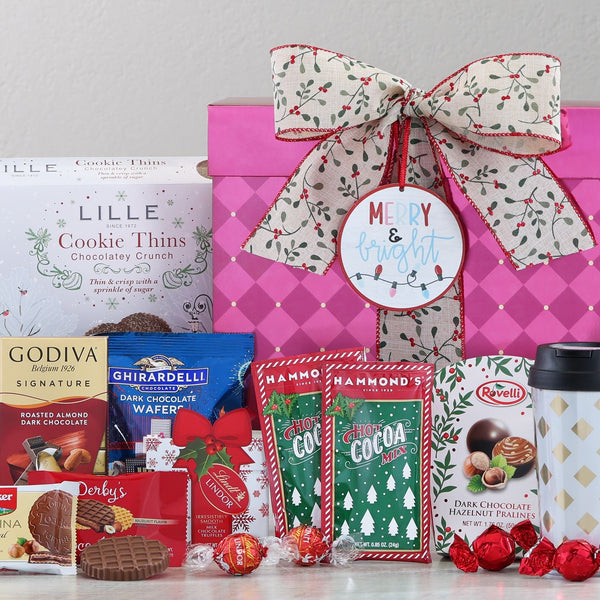 Red holiday gift box with ribbon containing assorted chocolates, hot cocoa mix, and travel mug